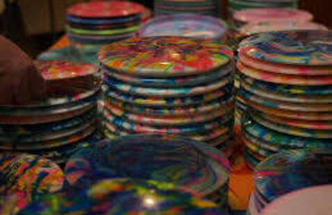 disc golf discs painted various colors and piled on a table.